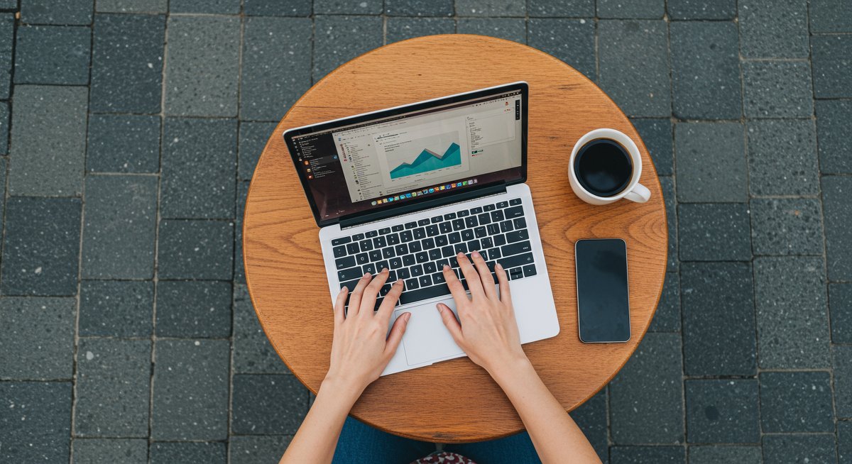 Minimalist mobile office setup featuring a laptop, portable monitor, and ergonomic mouse with a woman's hands typing in a clean modern design suitable for digital nomads